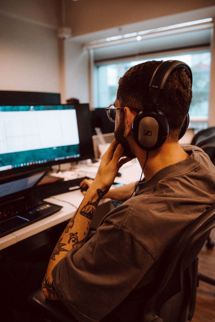The Art of Drawing Readers In: Your attractive post title goes here Young adult man focused on computer screen while wearing headphones in an office setting.
